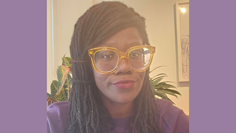 Portrait of Dr Yaz Iyabo Osho, Reader in Education and Director of Academic Professional Development, wearing glasses and smiling, seated indoors.